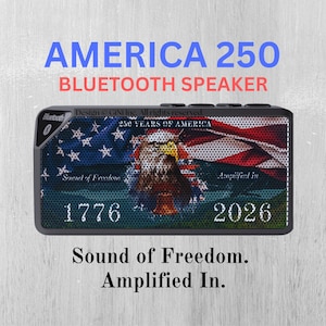 Op de afbeelding: Een rechthoekige Bluetooth-luidspreker met een patriottisch ontwerp. De luidspreker heeft een Amerikaanse vlag en een adelaarsafbeelding. Tekst op de luidspreker is onder meer "AMERICA 250", "1776" en "2026". De luidspreker heeft ook de woorden "Sound of Freedom. Amplified In."