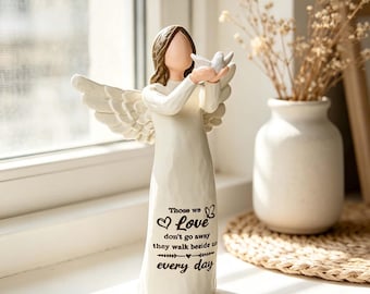 May include: A cream-colored angel figurine with brown hair and outstretched wings, holding a small white bird. The front of the gown features the black text: "Those we Love don't go away they walk beside us every day" with heart and butterfly icons.