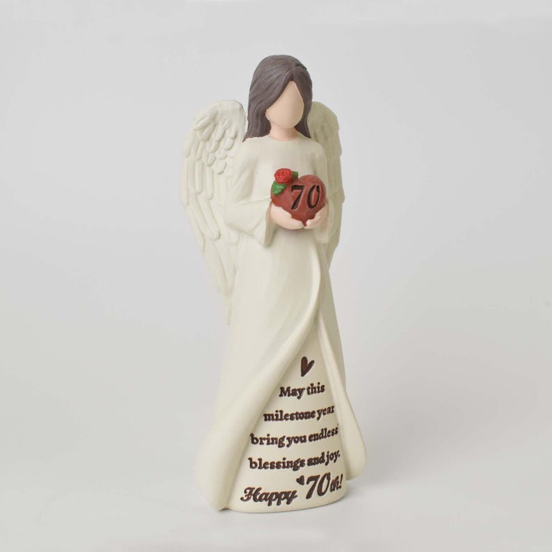 May include: A cream-colored angel figurine with brown hair and large wings, holding a red heart with the number 70 and a small rose. The dress features the text: May this milestone year bring you endless blessings and joy. Happy 70th!