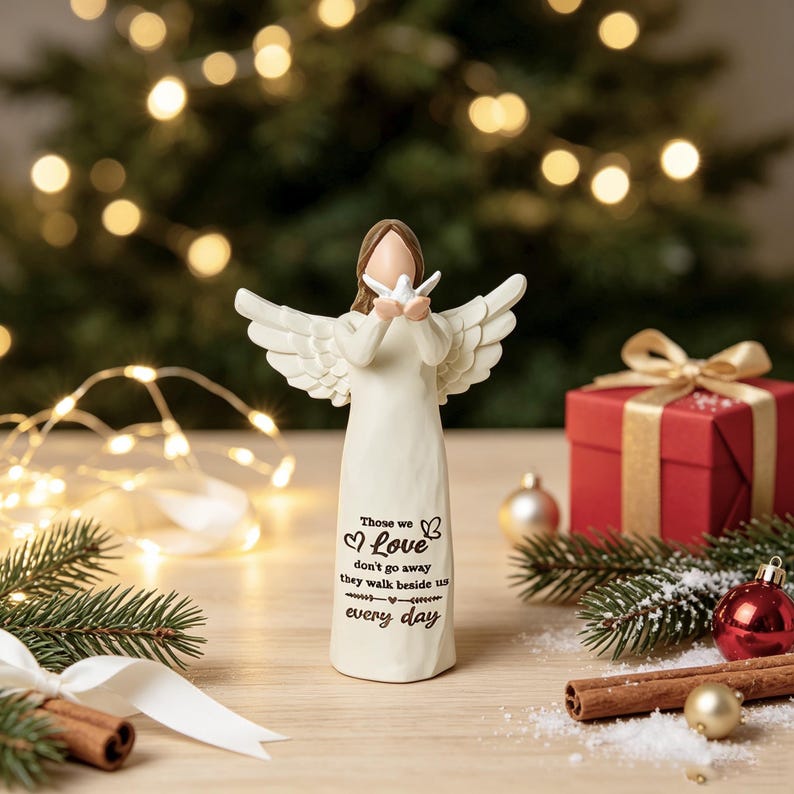 Christmas memorial angel figurine holding white dove, sympathy gift for loss of loved one, cream resin angel statue with quote Those we love don't go away, warm bokeh Christmas tree lights, pine branches, red gift box, baubles on wooden table, bereavement keepsake home decor