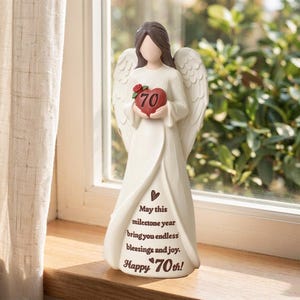 May include: A cream-colored angel figurine with brown hair and large wings, holding a red heart with the number 70 and a small rose. The dress features the text: May this milestone year bring you endless blessings and joy. Happy 70th!