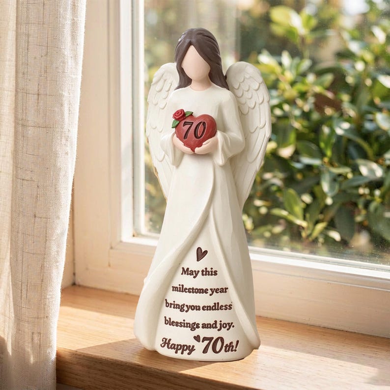 May include: A cream-colored angel figurine with brown hair and large wings, holding a red heart with the number 70 and a small rose. The dress features the text: May this milestone year bring you endless blessings and joy. Happy 70th!