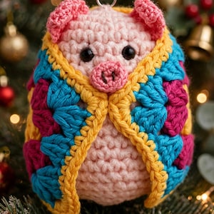 May include: A crocheted pig ornament featuring a light pink body with black eyes and a snout, wrapped in a colorful granny square blanket made of yellow, teal, and magenta yarn. The small handmade figure includes a metal loop at the top for hanging.