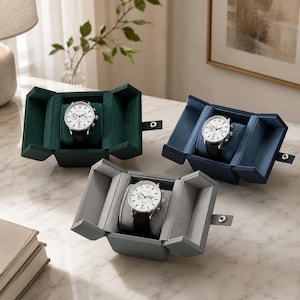 May include: Three wristwatches with white faces and black leather bands, each housed in an open, velvet-lined display box. The boxes are forest green, navy blue, and slate gray, featuring a snap-button closure on the side flap.