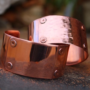 Pu&ograve; includere: Due braccialetti a polsino in rame. I braccialetti sono larghi, con una texture martellata su uno e una finitura liscia sull'altro. Ogni polsino ha diversi piccoli rivetti rotondi. Il rame ha una calda tonalit&agrave; marrone-rossastra.