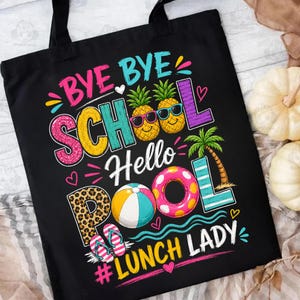 May include: Black tote bag with a colorful graphic design. The design includes the words "Bye Bye School Hello Pool Lunch Lady" with images of pineapples, a beach ball, a pool float, and flip-flops. The bag has black handles.