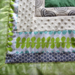 May include: A green, white, and blue baby blanket with a leafy pattern and polka dots. The blanket has a green satin border.