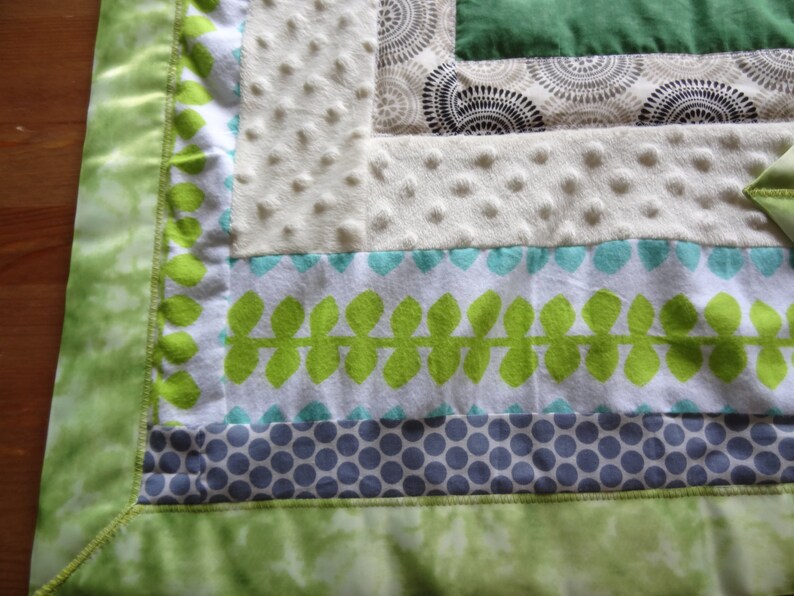May include: A green, white, and blue baby blanket with a leafy pattern and polka dots. The blanket has a green satin border.