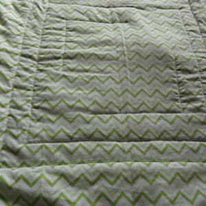 May include: A green and white chevron patterned quilt with a quilted design. The quilt has a white border and is made of a soft, comfortable fabric.