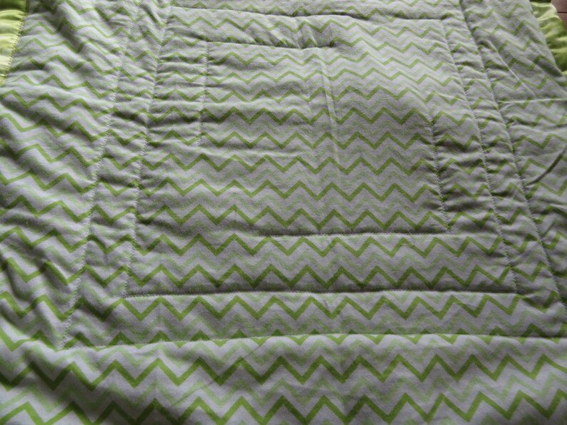 May include: A green and white chevron patterned quilt with a quilted design. The quilt has a white border and is made of a soft, comfortable fabric.