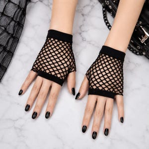 Pode incluir: Um par de luvas pretas sem dedos de rede com um padr&atilde;o de malha em forma de diamante e faixas de tecido preto s&oacute;lido no pulso e nos n&oacute;s dos dedos. As luvas cobrem as costas da m&atilde;o, deixando os dedos e o polegar completamente expostos.