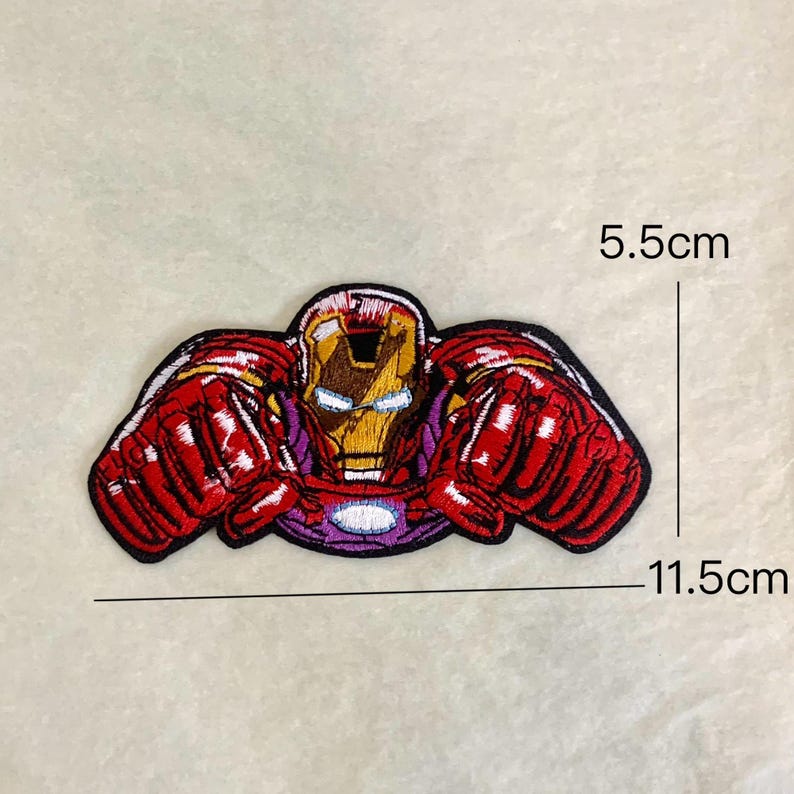 Op de afbeelding: Geborduurde Iron Man-patch met een gedetailleerd ontwerp van de helm en het pantser van de superheld. De patch is voornamelijk rood, goud en paars, met afmetingen van ongeveer 11,5 cm breed en 5,5 cm hoog.