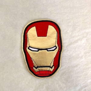 Op de afbeelding: Geborduurde patch met het Iron Man-masker. De patch heeft een gouden gezicht, rode accenten en een zwarte rand. De ogen zijn wit. Geschikt voor kleding, tassen of andere stoffen items.