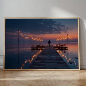 May include: A framed print depicting a tranquil sunset. A figure walks along a wooden pier over still water. Fairy lights are strung above the pier. The sky transitions from dark blue to orange and pink hues.
