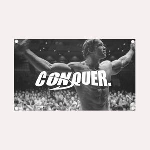 Peut inclure: Image en noir et blanc d'un bodybuilder levant les bras devant une foule. Le mot "CONQUER" est écrit en blanc sur l'image. Il s'agit d'une affiche de motivation.