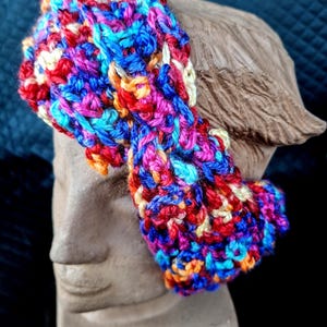 Puede incluir: Una colorida diadema tejida a mano con una vibrante mezcla de hilos rojos, azules, rosas y amarillos. La diadema se muestra sobre un busto, mostrando su textura y diseño. Este accesorio es perfecto para añadir un toque de color a cualquier atuendo.