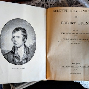 May include: An open book featuring a portrait of Robert Burns on the left page and the title page of "Selected Poems and Songs of Robert Burns" on the right. The book was edited by Philo Melvyn Buck, Jr. and published in 1916 by The Macmillan Company.