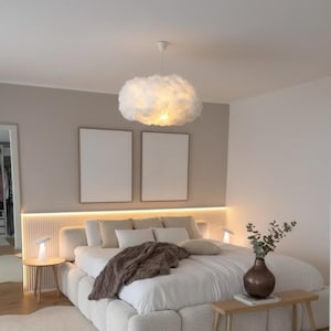 Peut inclure: Chambre moderne avec un grand lit, une couette et des oreillers blancs, une couverture marron et une suspension en forme de nuage. Deux toiles encadrées et vierges sont accrochées au-dessus du lit. Petites tables de chevet avec lampes.
