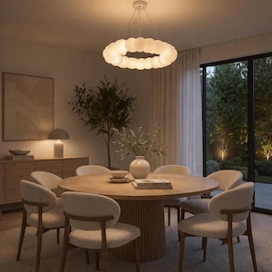 May include: A modern dining room featuring a round wooden table surrounded by six upholstered chairs. A white, circular chandelier hangs above the table. A large window offers a view of a well-lit outdoor space.