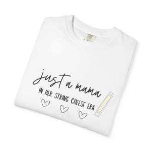 May include: White t-shirt with the text "just a mama in her string cheese era" in black script. The design includes three small hearts and a string cheese illustration.