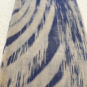 May include: A rectangular textile piece featuring a woven pattern of dark blue and beige vertical stripes. The design displays a blurred, ikat-style effect where the deep blue pigment transitions into the natural beige base, creating a soft, organic appearance across the fabric surface.