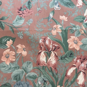 May include: A floral fabric with a repeating pattern of large flowers and foliage. The flowers are in shades of peach, pink, and white, with green leaves and stems. The background is a muted reddish-brown color.