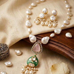 Puede incluir: Un conjunto de collar y pendientes con perlas barrocas blancas, un colgante triangular de cuarzo rosa y un dije de esmalte verde en forma de l&aacute;grima con motivo de loto. La joyer&iacute;a incluye peque&ntilde;as perlas colgantes y detalles met&aacute;licos dorados.