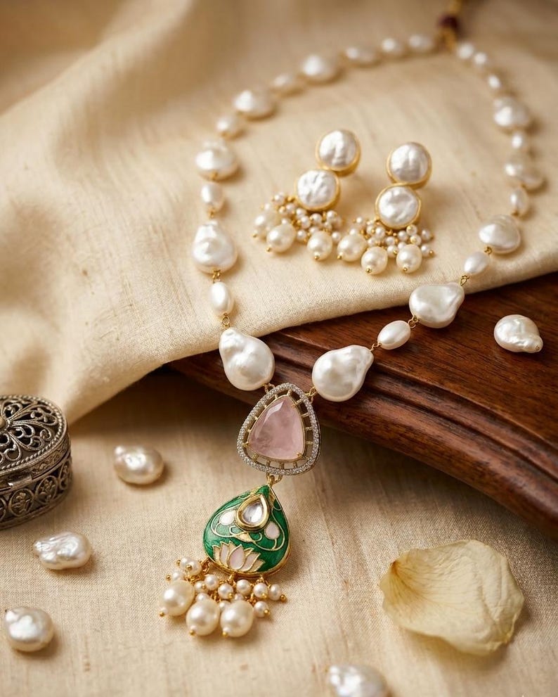 Puede incluir: Un conjunto de collar y pendientes con perlas barrocas blancas, un colgante triangular de cuarzo rosa y un dije de esmalte verde en forma de l&aacute;grima con motivo de loto. La joyer&iacute;a incluye peque&ntilde;as perlas colgantes y detalles met&aacute;licos dorados.