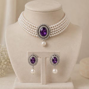 May include: A pearl necklace and earring set displayed on a mannequin. The necklace features multiple strands of white pearls, a large oval purple gemstone, and a dangling pearl. The earrings have matching purple gemstones and dangling pearls.