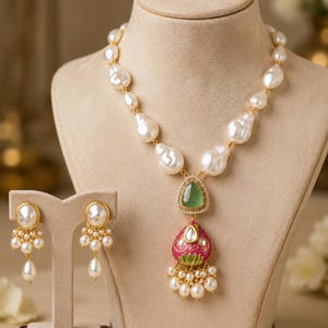 Puede incluir: Un conjunto de collar y pendientes con perlas barrocas blancas. El collar tiene un colgante central con una piedra verde, una forma de gota esmaltada en rosa y peque&ntilde;as perlas colgantes. Los pendientes cuentan con una perla y perlas peque&ntilde;as.