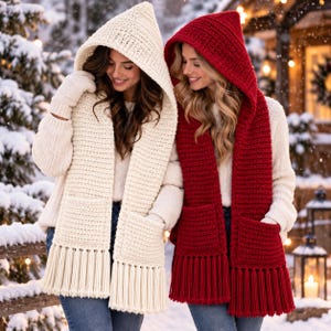 May include: Two hooded scarves, one cream and one deep red, featuring a chunky crochet knit texture, integrated pockets on each end, and long, thick fringe detailing. Each scarf is worn over a white sweater and blue jeans in a snowy setting.
