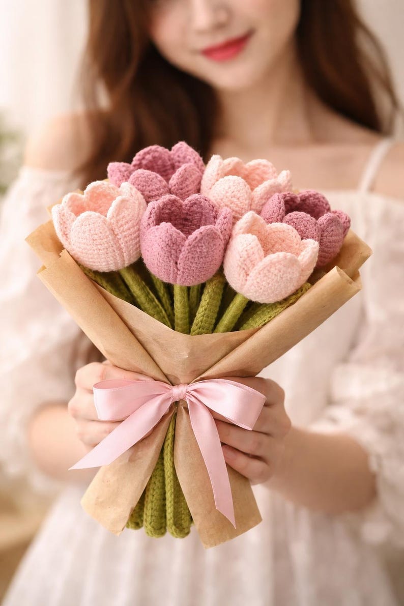May include: A bouquet of handmade crochet tulips in shades of pink and purple, wrapped in brown paper and tied with a pink satin ribbon. The stems are green.