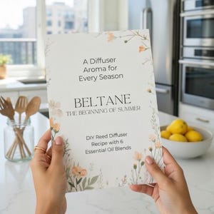 Può includere: Una persona tiene in mano una carta con accenti floreali e il testo "A Diffuser Aroma for Every Season" e "BELTANE THE BEGINNING OF SUMMER". La carta menziona anche una ricetta per diffusore a lamelle fai-da-te con 6 miscele di oli essenziali. Una ciotola di limoni e utensili di legno sono sullo sfondo.