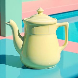 May include: A pale yellow ceramic teapot with a lid and handle. The teapot is set against a backdrop of pink and teal geometric shapes and a blue surface. The teapot's design is simple and elegant, with a curved spout and a rounded body.