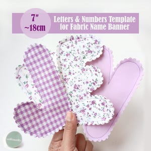 May include: Fabric name banner letters and numbers template. The template is 7 inches (approx. 18 cm) in size. The letters are made of fabric with floral and gingham patterns, and scalloped edges. The banner is designed for crafting.