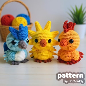 May include: Three colorful crochet bird figures. The first is blue and white, the second is yellow with star-like features, and the third is orange and red. A basket with yarn balls is in the background. The text "pattern by VinCrafty" is at the bottom.