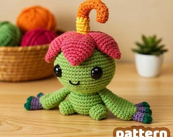 May include: A handmade green crochet creature with a flower-like head in shades of pink, yellow, and orange. It has large black eyes and outstretched arms with purple and green accents. The text "pattern by VinCrafty" is visible.