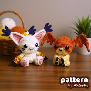 May include: Two crocheted Digimon figures. One is white with pink and blue accents, the other is orange and yellow. They have large ears and wings. The figures are sitting on a wooden surface. The text "pattern by VinCrafty" is in the bottom right corner.