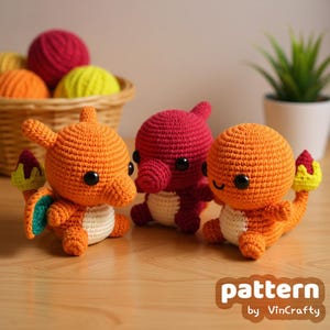 Könnte beinhalten: Drei gehäkelte orangefarbene und rote Charmander-Plüschtiere mit schwarzen Augen und weißen Bäuchen. Die Plüschtiere haben kleine Schwänze mit Flammen. Das Bild enthält auch einen Korb mit Wollknäueln und den Text "pattern by VinCrafty".