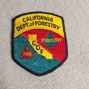 Op de afbeelding: Geborduurde patch met de tekst "CALIFORNIA DEPT. of FORESTRY" in geel, met een rood en groen ontwerp. De patch bevat de letters "CDF" en een driehoek met het woord "FIRE".