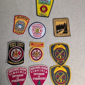 Op de afbeelding: Een verzameling geborduurde patches met verschillende ontwerpen en tekst. Patches zijn onder meer emblemen van de brandweer, een BSA Jamboree-patch en patches voor de Virginia Division of Forestry. Kleuren zijn rood, geel, blauw en wit.