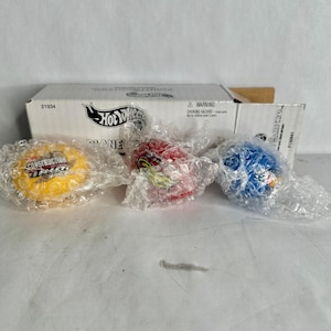 May include: Three Hot Wheels Planet Micro racers in bubble wrap packaging. One yellow, one red, and one blue. The yellow racer has "Construction Zone" text. The box behind the racers has the Hot Wheels logo and the number 21934.