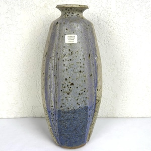 May include: A tall, handcrafted ceramic vase with a speckled gray and blue glaze. The vase features a flared top and a textured, dark blue base. A small label reads "Silverton Mountain Pottery Colorado."