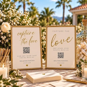 Op de afbeelding: Twee goudkleurige bordjes met een witte achtergrond voorzien van de tekst capture the love, een QR-code en de namen Mr & Mrs Martina met de datum 18.08.2028. De bordjes bevatten onderaan in het midden een klein gouden hartsymbool.