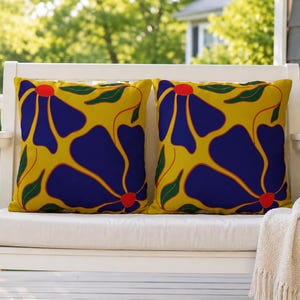 May include: Two square throw pillows featuring a bold, repeating floral pattern. The design consists of large, deep blue petals with bright red centers set against a vibrant yellow background, accented by small, dark green leaves.