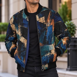 May include: A bomber jacket featuring a black base with abstract brushstroke patterns in shades of blue, teal, and metallic gold. The jacket has a black ribbed collar, black ribbed cuffs, and a front zipper closure, worn over a plain black shirt.