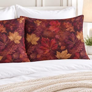 May include: Two rectangular pillowcases featuring a vibrant autumn-themed pattern of fallen maple and oak leaves in shades of deep red, burnt orange, and golden yellow against a dark, moody background, displayed on a white bed set.