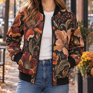 May include: A black bomber jacket featuring a vibrant floral pattern in shades of orange, rust, and gold. The jacket has a black ribbed collar, cuffs, and hem, a front zip closure, and two side pockets, worn over a white shirt and blue jeans.