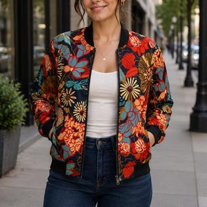 Può includere: Un giubbotto bomber con base blu scuro e un vivace motivo floreale nei toni del rosso, arancione, giallo e verde acqua. Il giubbotto presenta un colletto a coste nero, polsini a coste neri e una chiusura frontale con cerniera.