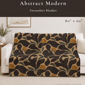 May include: An abstract modern sweatshirt blanket measuring 80 inches by 60 inches. The blanket features a repeating pattern of dark brown, muted teal, and mustard yellow organic shapes on a tan background, draped over a white sofa.